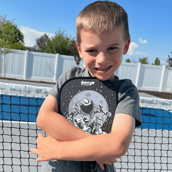 Kids pickleball paddle with astronaut design being held by a kid on a pickleball court