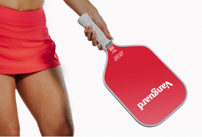 Vanguard red pickleball paddle with white handle held by a person wearing a red skirt on a white background