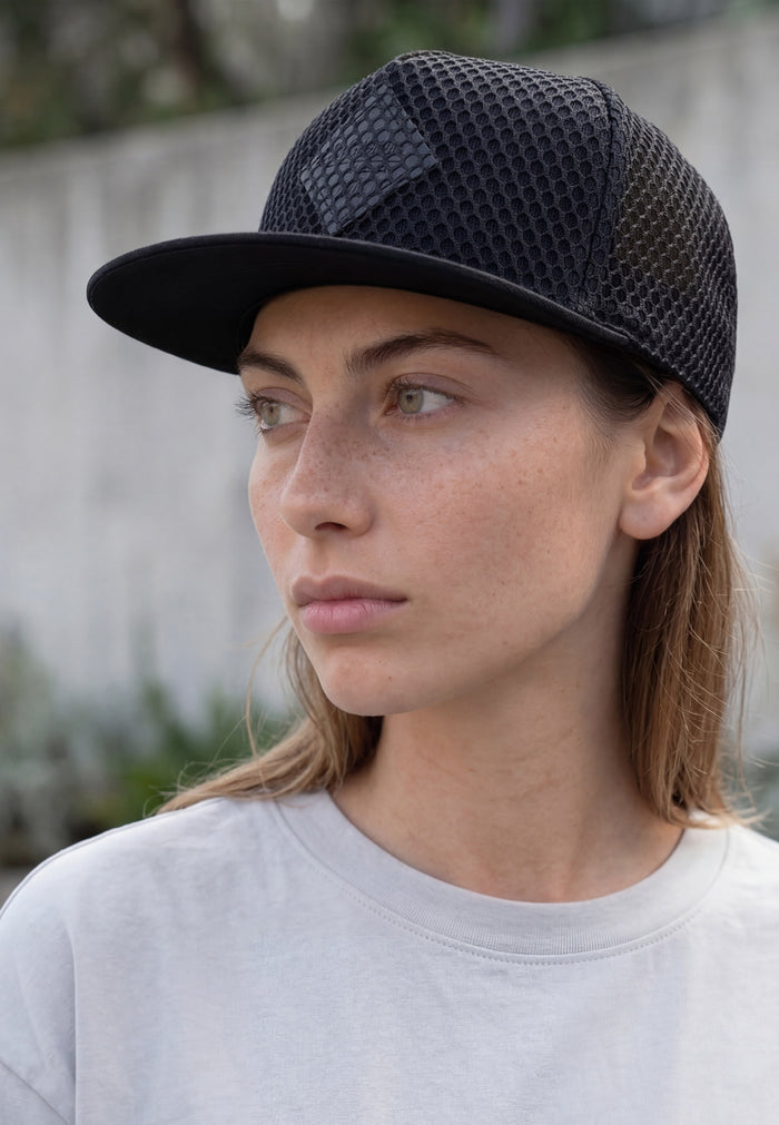 Woman wearing a black cap with mesh and gray sweatshirt outdoors