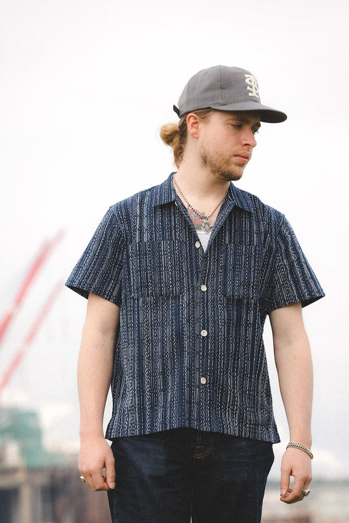 Man wearing a blue patterned shirt and gray cap outdoors