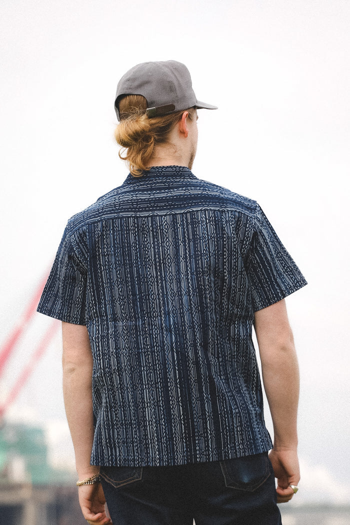 Person wearing a patterned shirt and cap with a blurred background