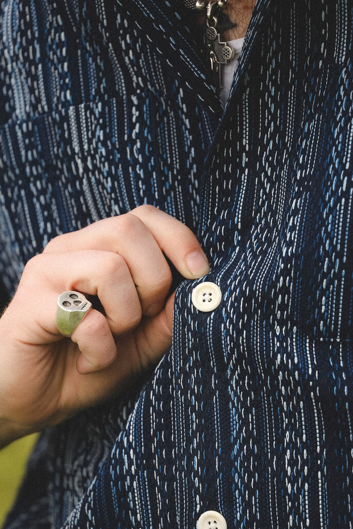 Close-up of a person buttoning a dark blue patterned jacket with a green ring on a blurred background.