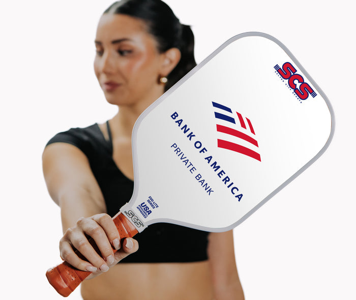 Woman holding a pickleball paddle with visible branding on a white background