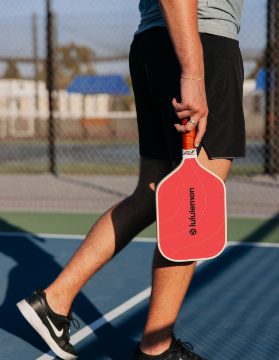 Person holding a red Lululemon pickleball paddle on a court