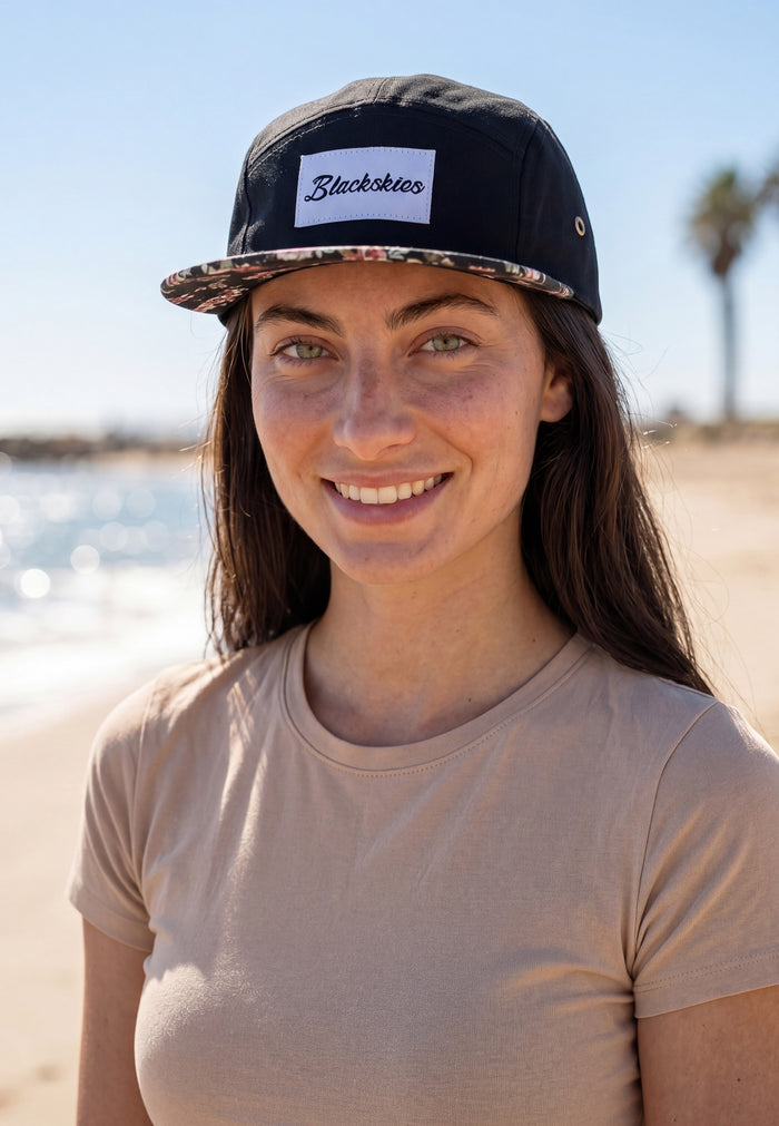 Woman wearing a cap with 'Blackskies' logo on a beach