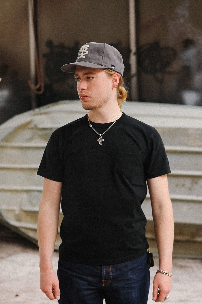 Man wearing a black t-shirt and gray cap standing in front of a blurred background