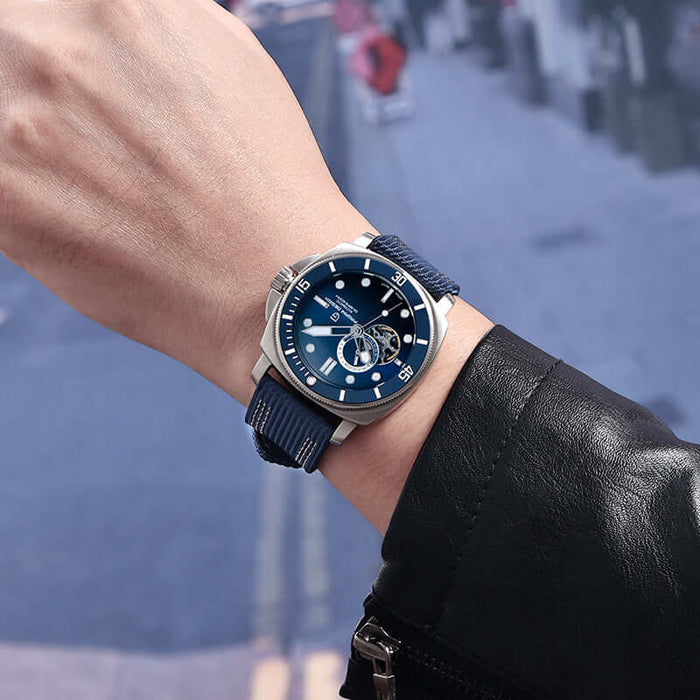 Fully Automatic Mechanical Watch With Luminous Display on a man's wrist with a blue strap in a city background.