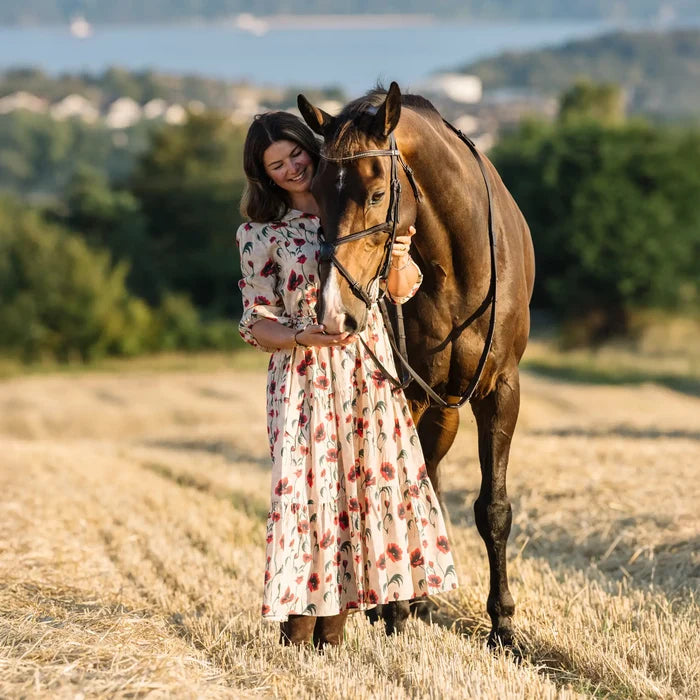 Woman in a floral dress standing next to a horse in a field with a scenic background