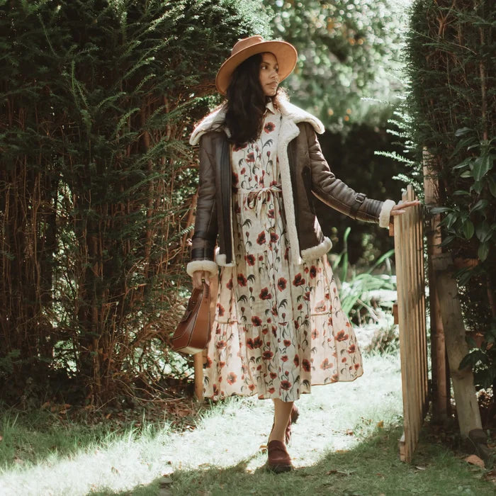 Woman in a floral dress and hat standing in a garden