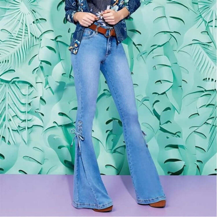Model wearing Mid Waisted Stretch Denim Flare Jeans against a tropical leaf background, showcasing stylish and modern denim fashion.