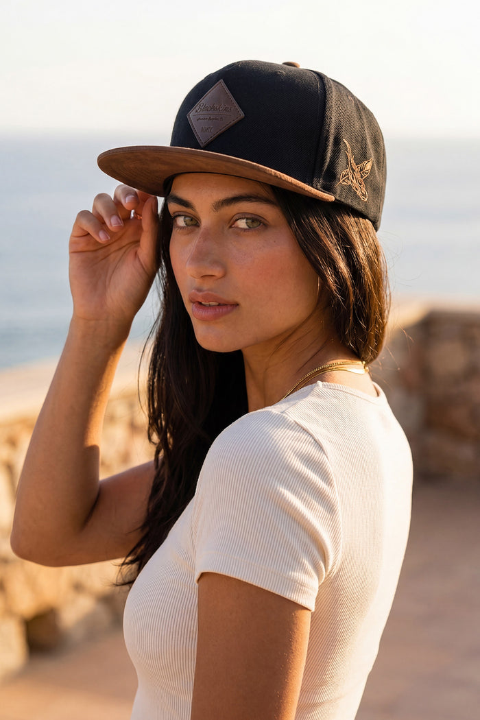 Woman wearing a black brown blackskies snapback cap with a logo on a beach