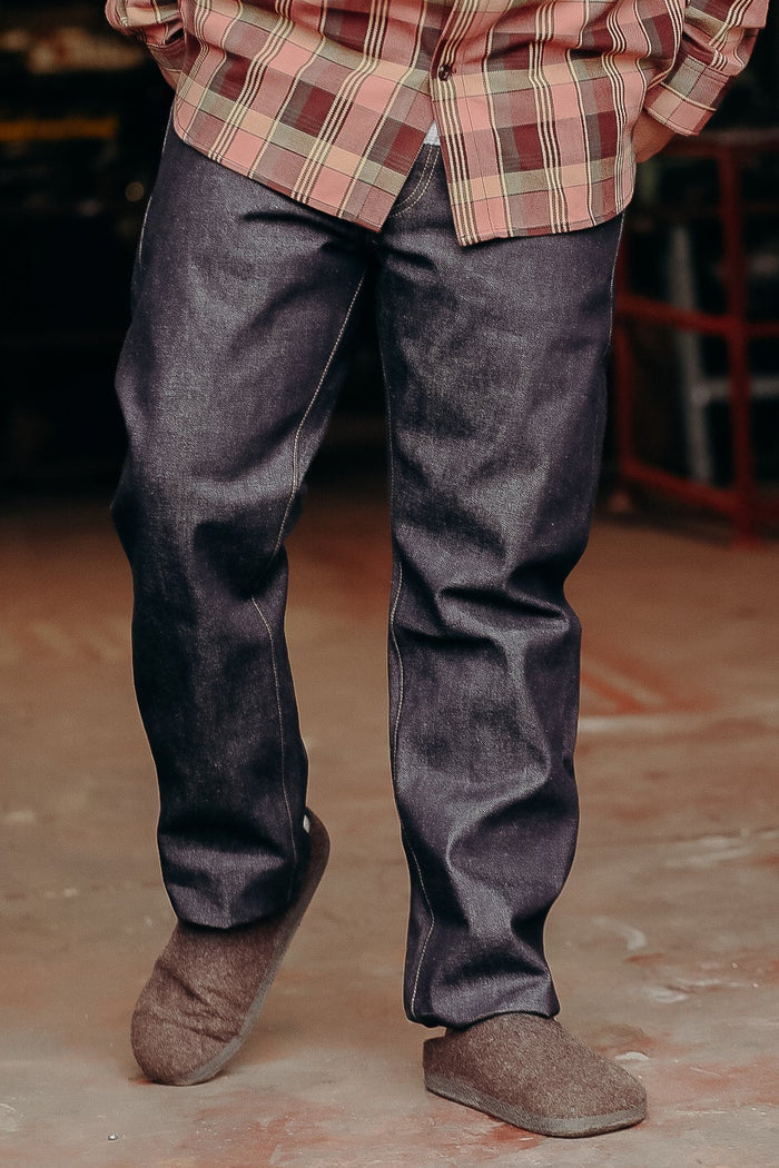 Person wearing dark denim jeans, plaid shirt, and gray wool slippers on concrete floor