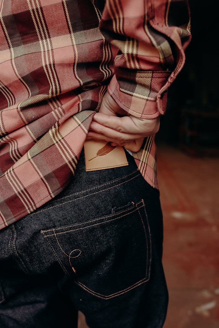 Person in red plaid shirt putting leather wallet with feather logo into dark denim jeans pocket