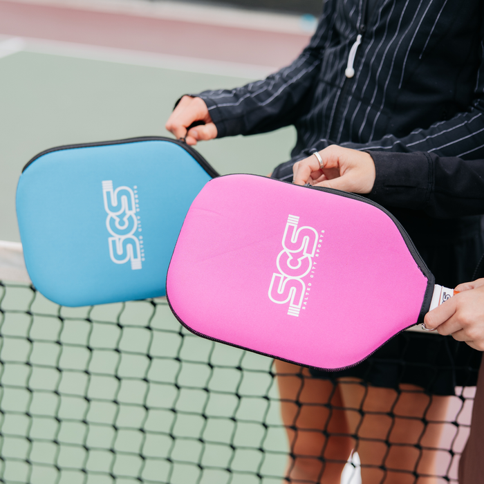 Two pickleball paddles, one blue and one pink, held by a person on a court.