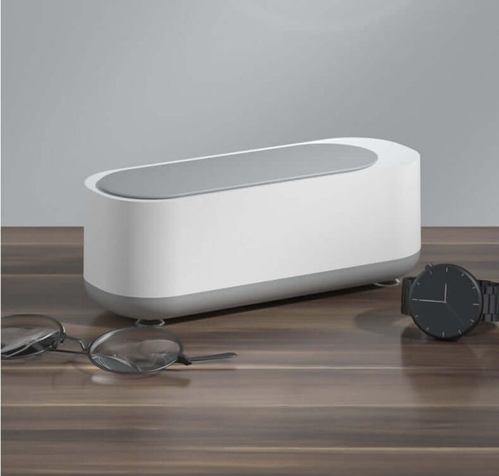 Ultrasonic High Frequency Jewelry and Glasses Cleaner on a wooden table with glasses and a watch.