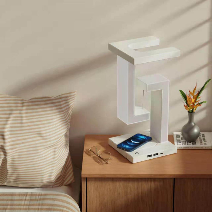 Wireless Charging Suspension Magnetic Table Lamp on a bedside table with a blue phone and decorative plant.